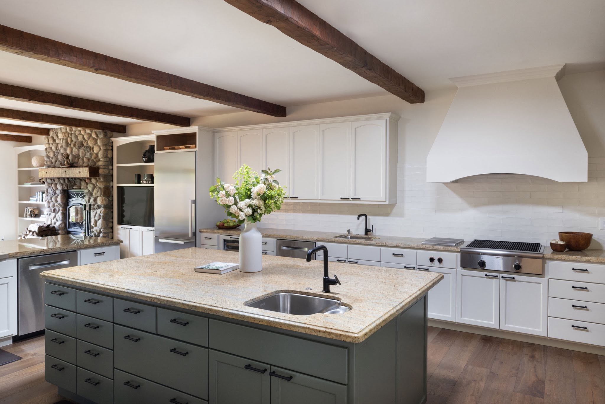 Kitchen island with wood beams and stone fireplace beyond